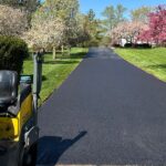 Freshly paved residential asphalt driveway lined with blooming spring trees, completed by OZ Paving during Colorado's ideal spring paving season